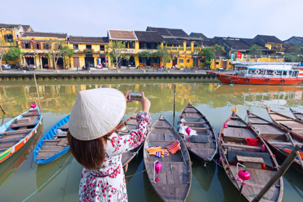 Woman tourist with wearing Vietnamese Non La hat is taking photograph of Ancient heritage Hoi An city during travel in Vietnam.